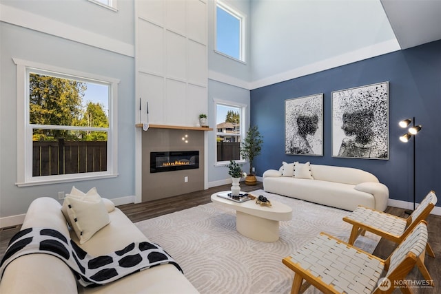 living area with wood finished floors, a glass covered fireplace, baseboards, and a high ceiling