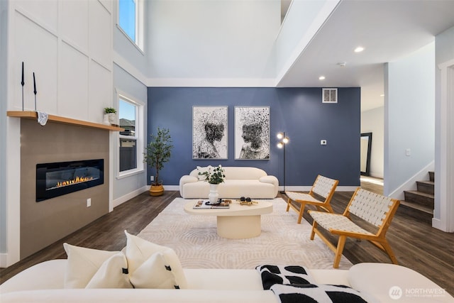 living area featuring wood finished floors, a glass covered fireplace, recessed lighting, baseboards, and stairway