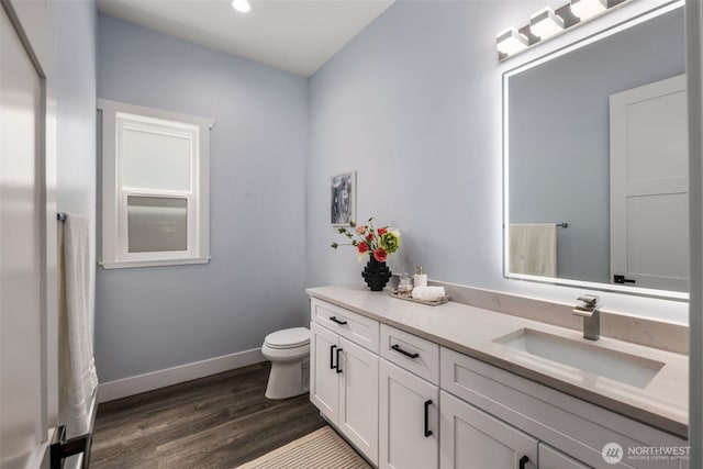 bathroom with wood finished floors, toilet, vanity, baseboards, and recessed lighting