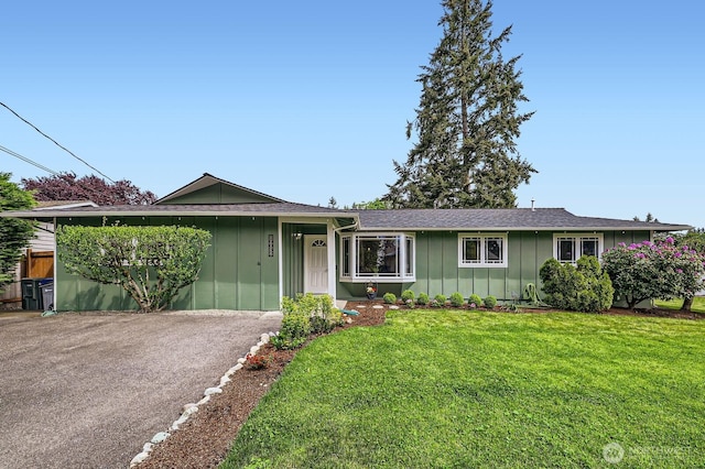 ranch-style home with board and batten siding, a front lawn, and a shingled roof