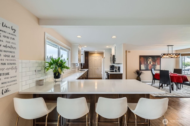 kitchen with stainless steel appliances, wood finished floors, light countertops, a kitchen breakfast bar, and tasteful backsplash