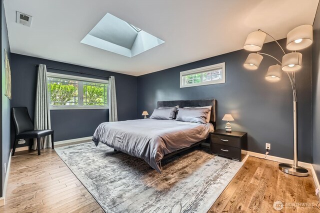 bedroom with a skylight, light wood-style flooring, and baseboards