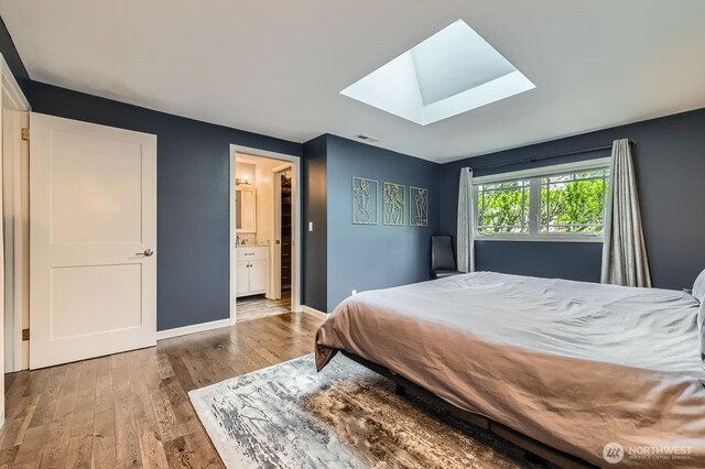 bedroom featuring a skylight, wood finished floors, baseboards, and connected bathroom