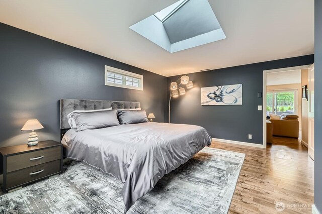 bedroom with wood finished floors, a skylight, and baseboards