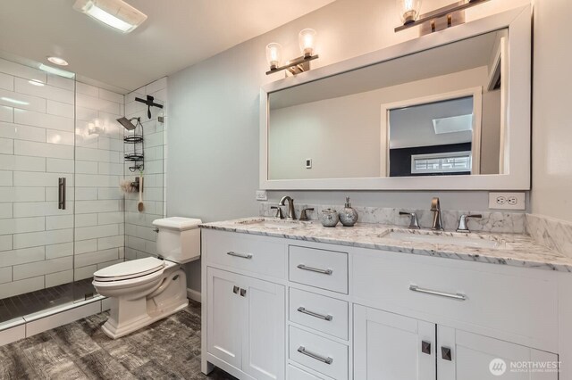 bathroom with toilet, a stall shower, double vanity, and wood finished floors