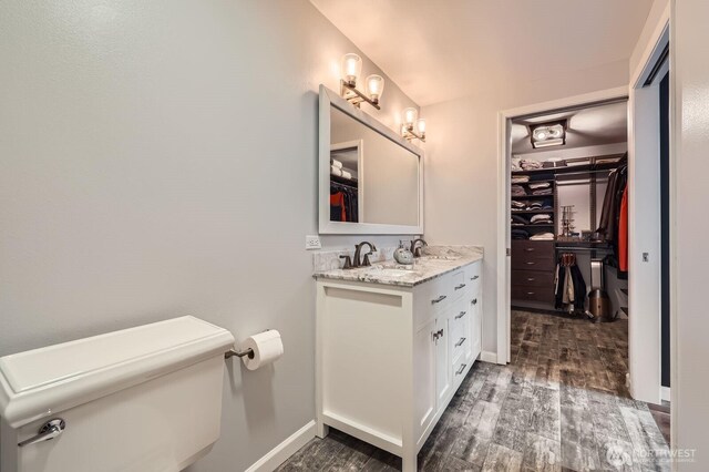 bathroom featuring wood finished floors, a spacious closet, vanity, toilet, and baseboards