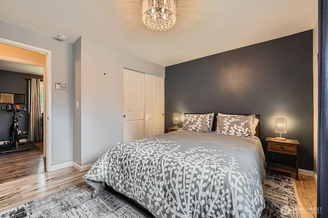 bedroom with wood finished floors, baseboards, a closet, and a chandelier