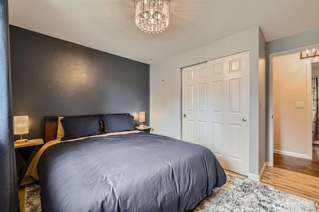 bedroom with a chandelier, wood finished floors, baseboards, and a closet