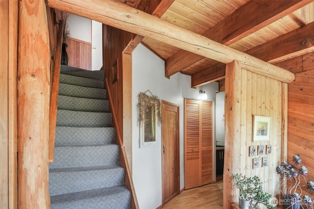 stairs featuring wood finished floors, beamed ceiling, wood ceiling, and wood walls