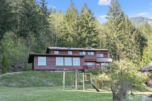 back of property with a playground, a yard, and a forest view