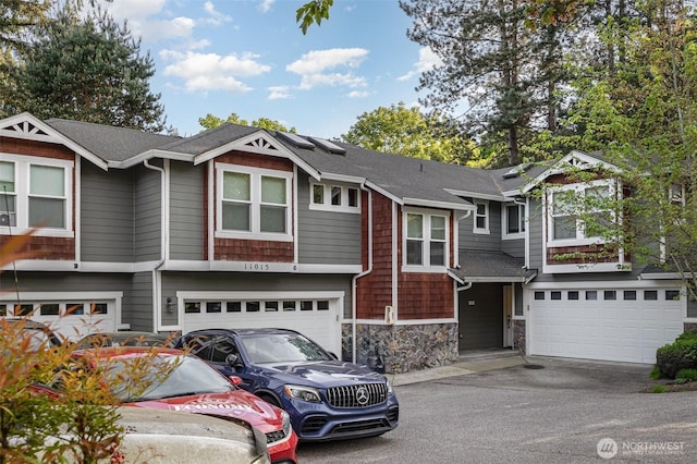 view of front of home with an attached garage, driveway, stone siding, and roof with shingles
