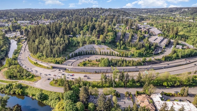 aerial view of property and surrounding area with a major roadway, a forest, and a nearby body of water