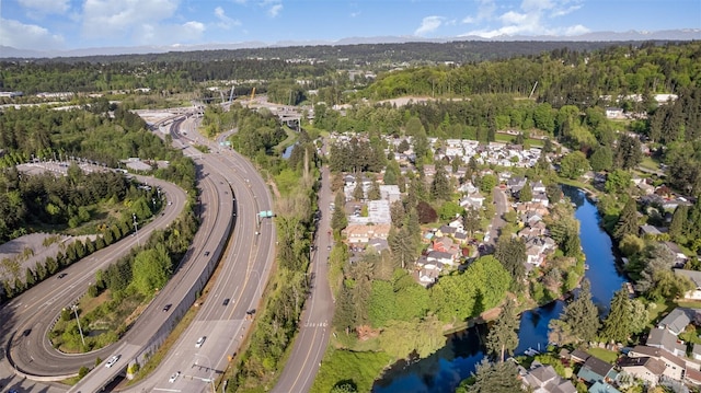 aerial view of property and surrounding area featuring a highway, a nearby body of water, and a heavily wooded area