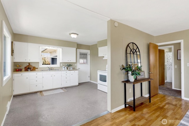 kitchen featuring baseboards, a sink, white electric range oven, light countertops, and white cabinets