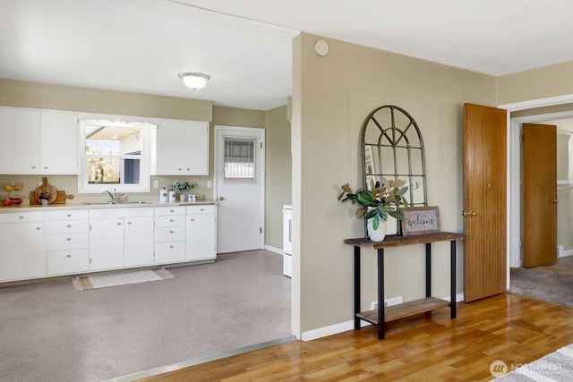 kitchen featuring white cabinetry, baseboards, light countertops, and a sink