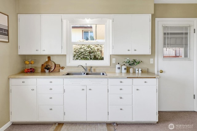 kitchen featuring white cabinets, light countertops, baseboards, and a sink