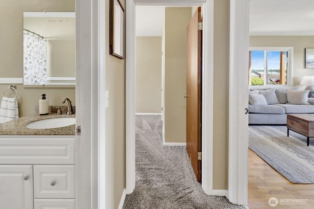 hallway featuring baseboards, light colored carpet, and a sink
