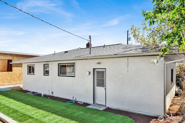 back of property with a lawn, stucco siding, and a shingled roof