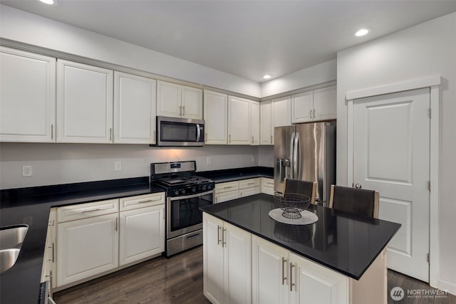kitchen with stainless steel appliances, dark countertops, dark wood-style flooring, white cabinets, and recessed lighting
