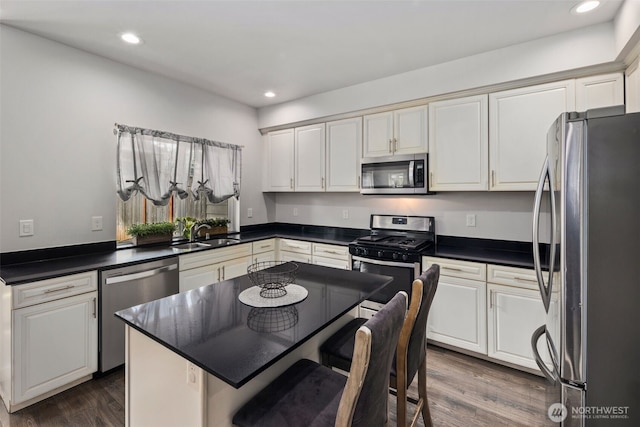 kitchen featuring stainless steel appliances, a sink, dark countertops, dark wood-type flooring, and white cabinets