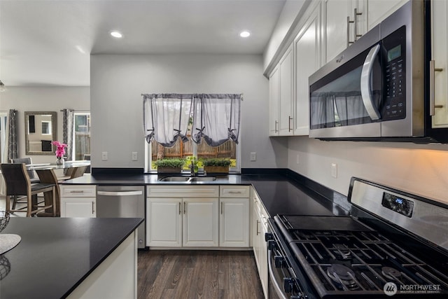 kitchen with appliances with stainless steel finishes, dark countertops, dark wood-type flooring, white cabinetry, and a sink