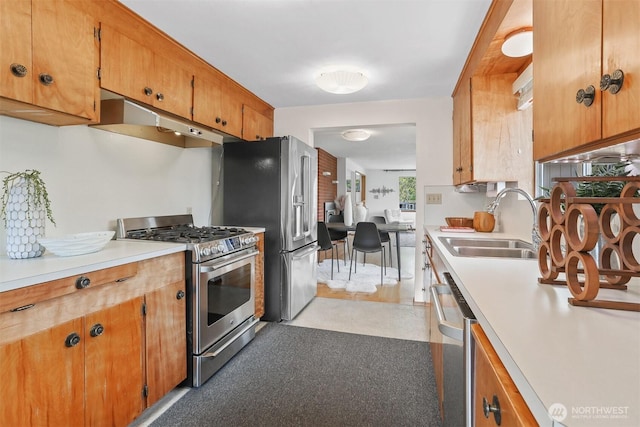 kitchen featuring appliances with stainless steel finishes, under cabinet range hood, a sink, light countertops, and brown cabinetry