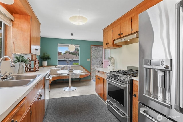 kitchen with stainless steel appliances, under cabinet range hood, a sink, brown cabinetry, and light countertops
