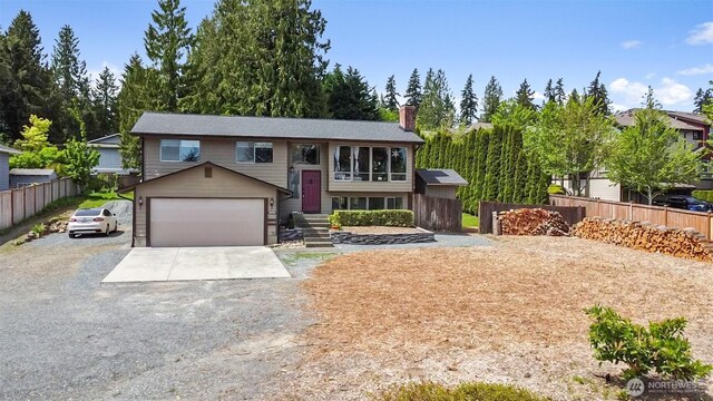 split foyer home with a chimney, fence, driveway, and a garage