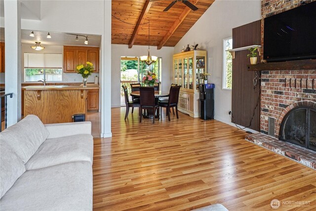 living room featuring light wood-style flooring, wood ceiling, a ceiling fan, a chandelier, and a brick fireplace
