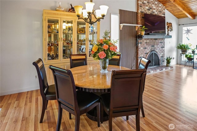 dining room featuring a chandelier, light wood-type flooring, wooden ceiling, a brick fireplace, and baseboards