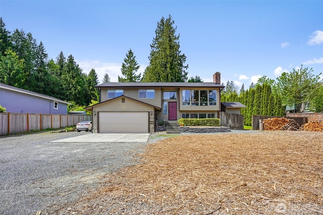 raised ranch featuring a chimney, driveway, fence, and a garage