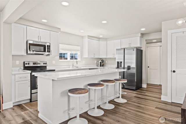 3342 Greenwood Ave W, University Place, WA 98466 - kitchen with appliances with stainless steel finishes, white cabinetry, wood finished floors, a kitchen breakfast bar, and recessed lighting