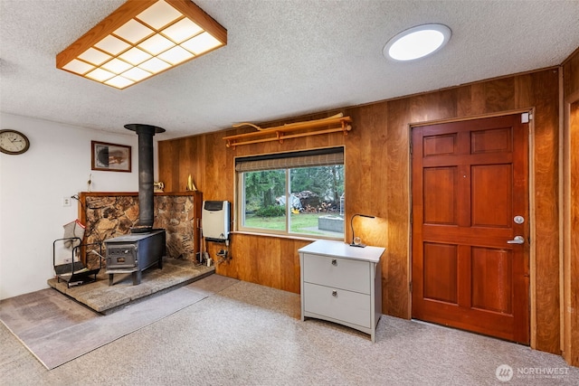 miscellaneous room featuring wooden walls, a textured ceiling, a wood stove, heating unit, and carpet floors