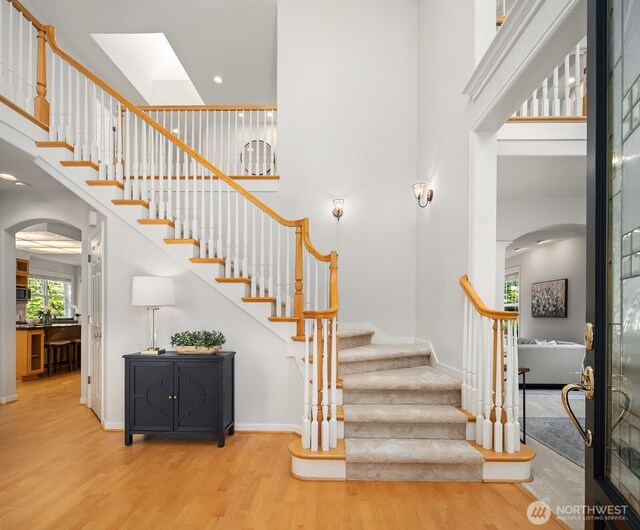 26108 SE 27th St, Sammamish, WA 98075 - staircase featuring arched walkways, a high ceiling, wood finished floors, a skylight, and baseboards