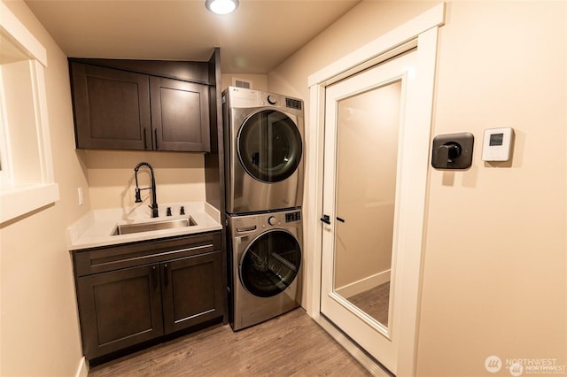 laundry area with stacked washer and clothes dryer, cabinet space, and light wood-type flooring