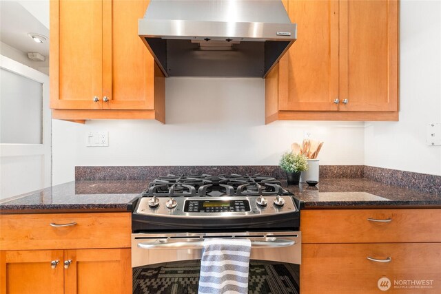 kitchen featuring stainless steel gas range, range hood, dark stone countertops, and brown cabinets