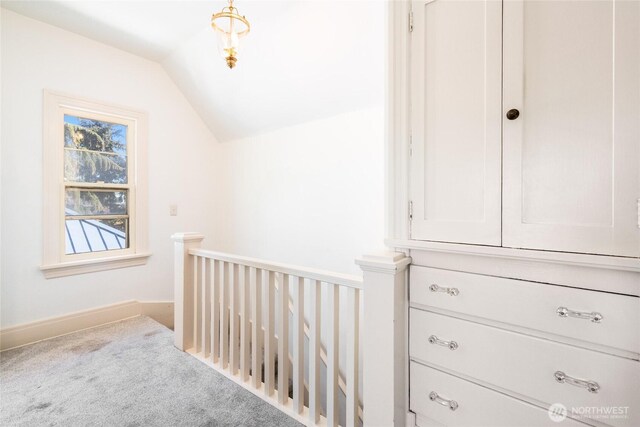 corridor with an upstairs landing, lofted ceiling, carpet, and baseboards