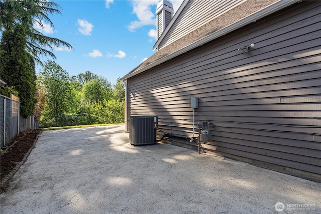 view of side of property featuring central AC unit, fence, a patio area, and a chimney
