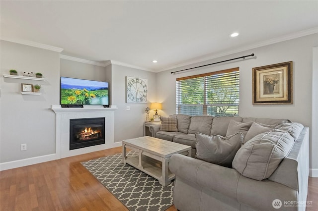 living area with wood finished floors, baseboards, crown molding, a glass covered fireplace, and recessed lighting