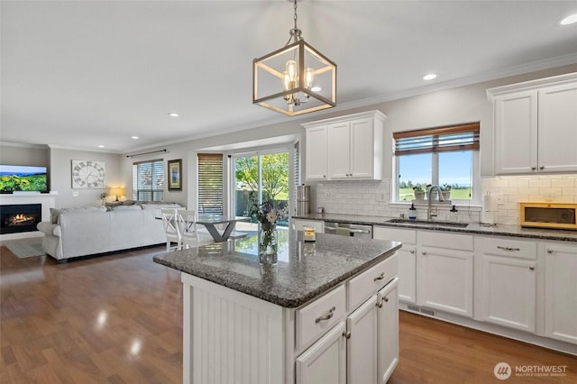 kitchen with a sink, a lit fireplace, plenty of natural light, dark wood-style flooring, and crown molding