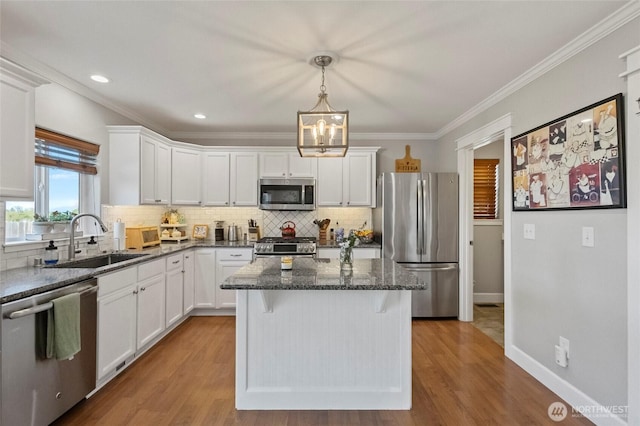 kitchen with appliances with stainless steel finishes, a sink, a center island, white cabinetry, and ornamental molding
