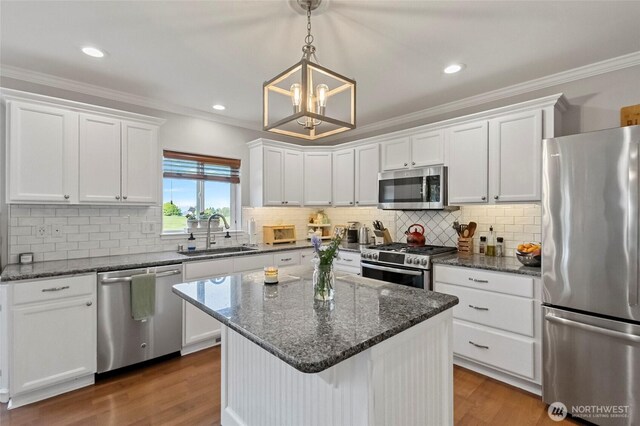 kitchen featuring appliances with stainless steel finishes, a sink, a chandelier, white cabinetry, and ornamental molding