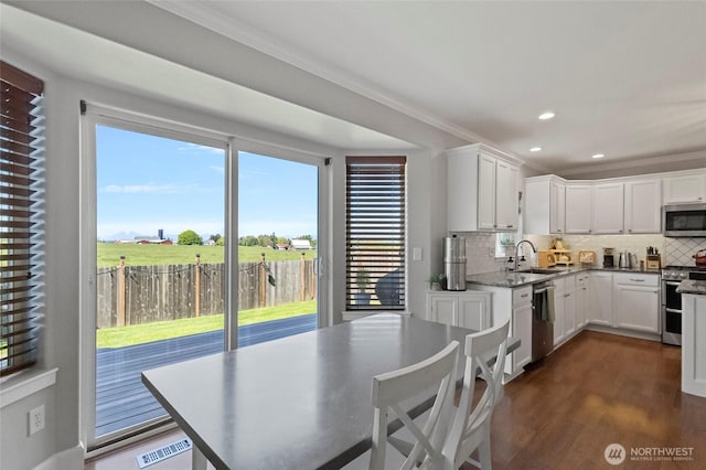 kitchen with stainless steel appliances, a sink, decorative backsplash, white cabinets, and ornamental molding