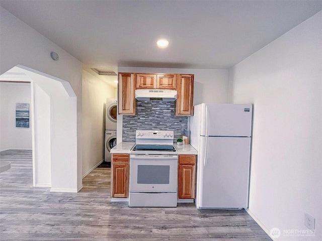 kitchen with white appliances, stacked washer / dryer, under cabinet range hood, backsplash, and light countertops