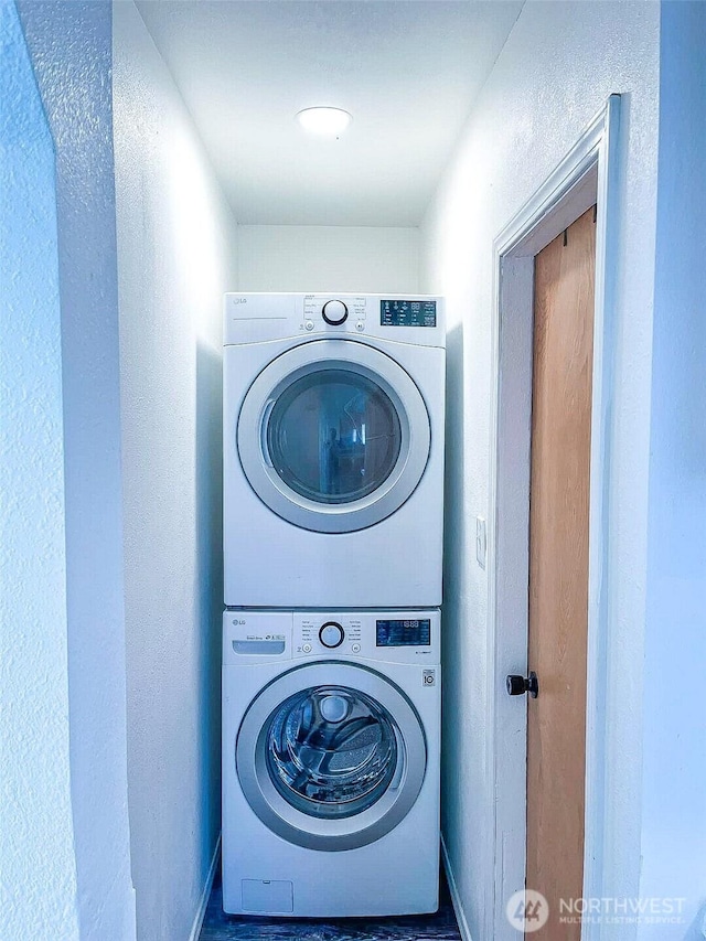 washroom featuring stacked washer and clothes dryer and baseboards