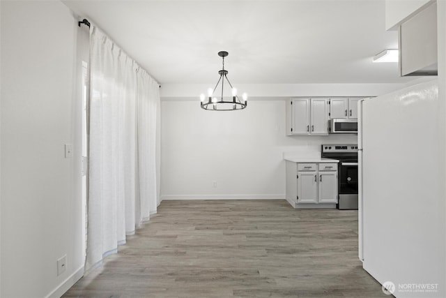 3121 W Hood Ave Unit E203, Kennewick, WA 99336 - kitchen with appliances with stainless steel finishes, a chandelier, baseboards, light wood-style flooring, and light countertops
