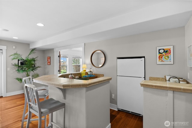 257 3rd Ave, Fox Island, WA 98333 - kitchen featuring freestanding refrigerator, tile counters, a breakfast bar area, dark wood-style floors, and baseboards