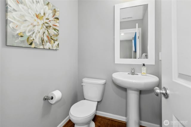 half bath featuring baseboards, toilet, wood finished floors, and a sink