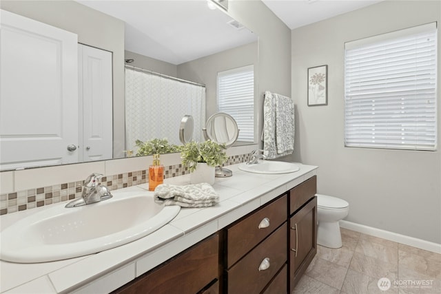 bathroom with baseboards, toilet, double vanity, and a shower with curtain