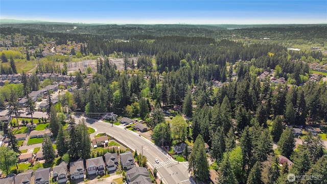 aerial view of property and surrounding area featuring a forest and nearby suburban area